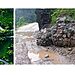 Aerial view of a winding road through green hills and a close-up of a muddy road with a gabion wall, illustrating the challenges of the Mechi Highway, particularly the Rajduwali landslide-prone section.